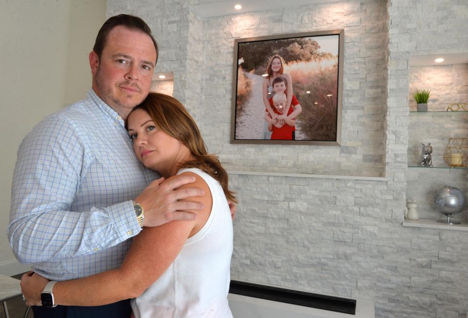 Paul and Sarah Alexander, pose for a photo at their home in Osprey, in front of a family portrait of Lilly Glaubach and her brothers. Lilly was killed last year after a car hit her as she was crossing Bay St. on her bike near Pine View School. 