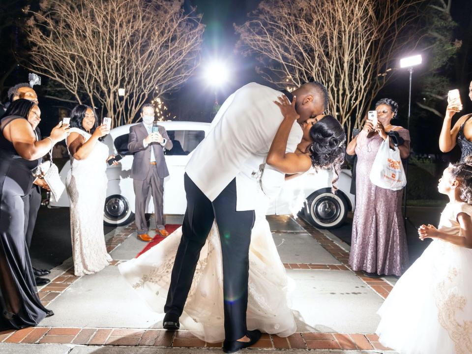 A groom dips and kisses his bride as their loved ones smile at them.