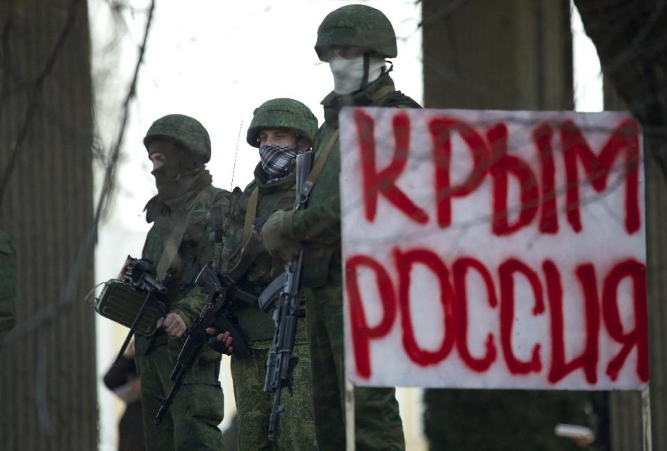 Un grupo de pistoleros no identificados en uniforme de camuflaje bloquea la entrada al Parlamento de Crimea en Simferopol, Ucrania, el sábado 1 de marzo del 2014. El cartel dice "Crimea Rusia". (AP Foto/Ivan Sekretarev)