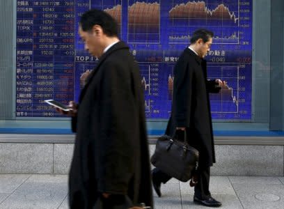 FILE PHOTO - Men walk past an electronic board showing market indices outside a brokerage in Tokyo, Japan,  March 2, 2016.    REUTERS/Thomas Peter