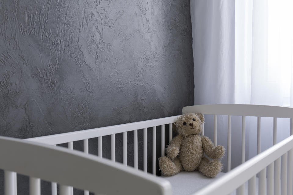 An empty baby crib with a stuffed animal in the corner.