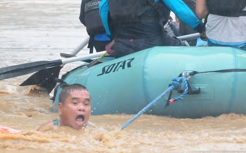 A man clings onto the rope of a rescue boat as residents are evacuated from their homes due to heavy flooding in Cagayan de Oro city in the Philippines - Credit: Froilan Gallardo/Reuters