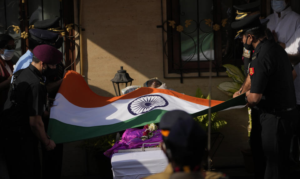 Defense forces put Indian flag on the body of Lata Mangeshkar, outside her home in Mumbai, India, Sunday, Feb.6, 2022. The legendary Indian singer with a prolific, groundbreaking catalog and a voice recognized by a billion people in South Asia, died Sunday morning of multiple organ failure. She was 92. (AP Photo/Rafiq Maqbool)