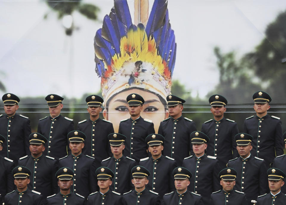 Newly graduated police cadets stand in formation in front of a large photograph of an indigenous police officer, during their graduation ceremony in Bogota, Colombia, Thursday, Nov. 7, 2019. (AP Photo/Fernando Vergara)