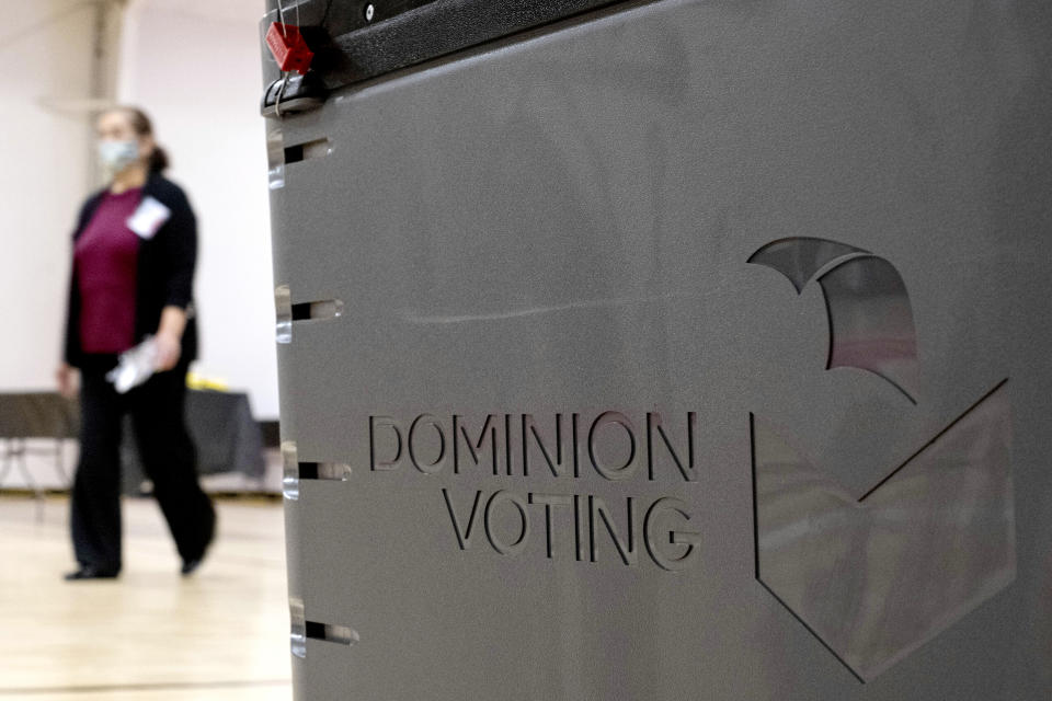 FILE - In this Jan. 4, 2021, file photo a worker passes a Dominion Voting ballot scanner while setting up a polling location at an elementary school in Gwinnett County, Ga., outside of Atlanta. Republican efforts to question the results of the 2020 election have led to two significant breaches of voting software that have alarmed election security experts who say they have increased the risk to elections in jurisdictions that use the equipment. (AP Photo/Ben Gray, File)