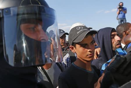 A riot policeman watches migrants as they wait for a bus near a collection point in Roszke village, Hungary September 9, 2015. REUTERS/Laszlo Balogh