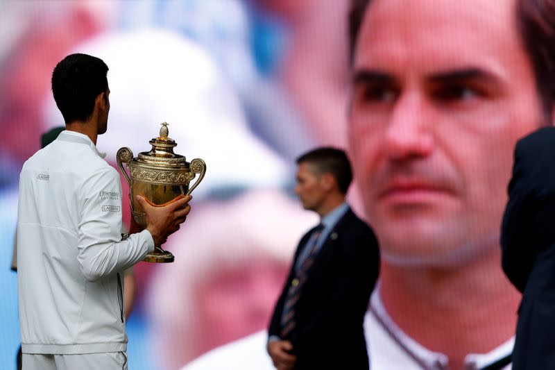 FILE PHOTO: Serbia's Novak Djokovic holds the Wimbledon trophy after winning the 2019 final as Switzerland's Roger Federer is on a screen in the background Wimbledon