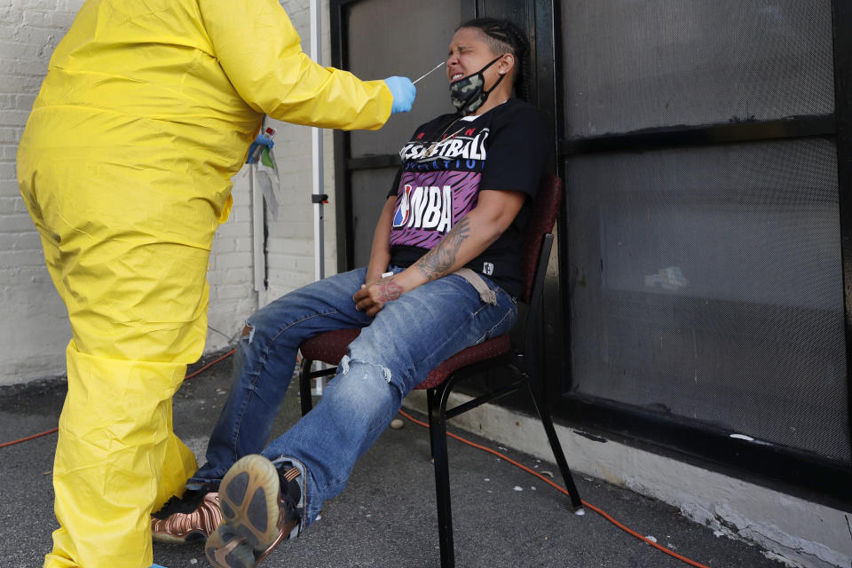 Naliber Tavares winces as she receives a COVID-19 test at the Whittier Street Health Center's mobile test site, Wednesday, July 15, 2020, in Boston's Dorchester section. The health center has administered free COVID-19 tests to over 5,000 people. The tests, administered since April 13, have been a popular service in Boston's low-income communities that have experienced high rates of infection. (AP Photo/Elise Amendola)