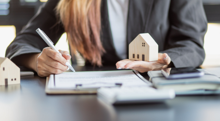 Woman hands holding home model, small miniature white toy house. Mortgage property insurance dream moving home and real estate concept. Case-Shiller, housing market.