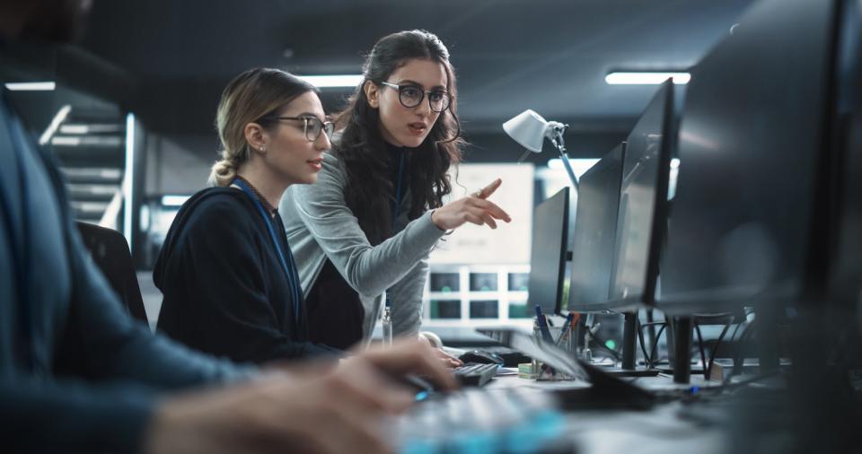 Two people looking at a computer monitor and talking.