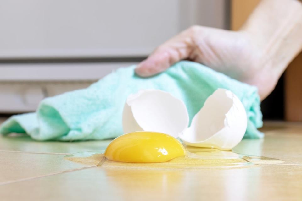 Wiping cracked egg off a tile floor with a towel.