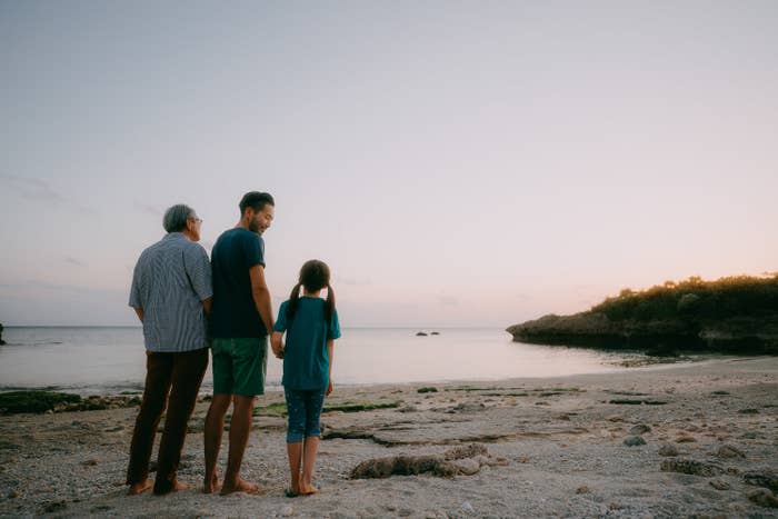 A grandfather, his son and granddaughter watch the sunset by the water