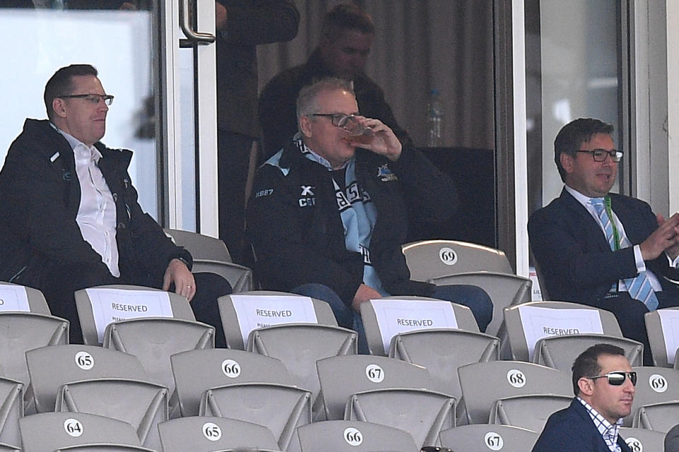 Prime Minister Scott Morrison sitting in the stands and drinking a beer while watching the Cronulla Sharks.