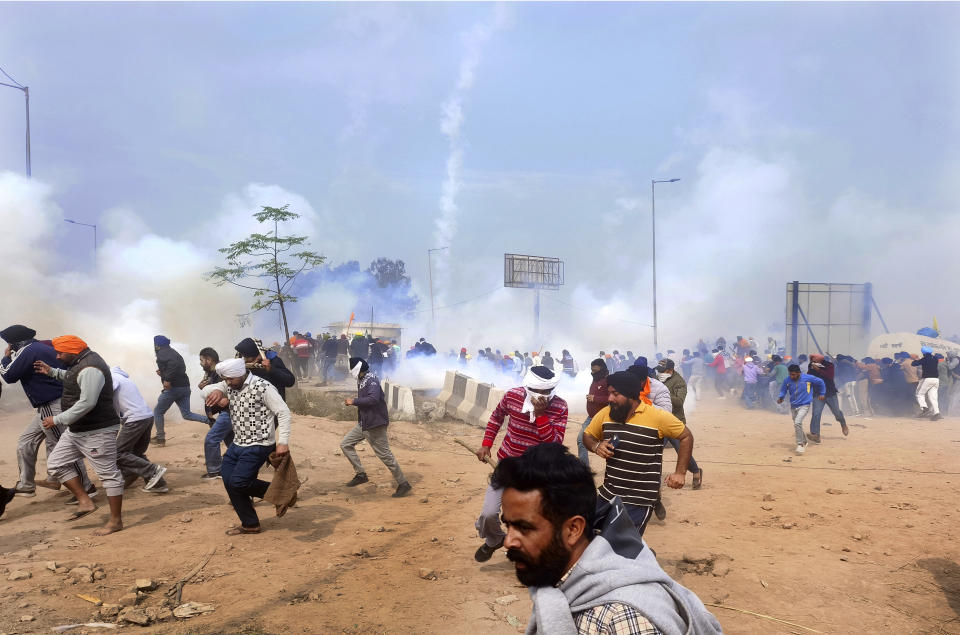 Farmers run for cover after police fired tear gas to disperse protesting farmers who were marching to New Delhi near the Punjab-Haryana border at Shambhu, India, Tuesday, Feb.13, 2024. Farmers are marching to the Indian capital asking for a guaranteed minimum support price for all farm produce. (AP Photo/Rajesh Sachar)