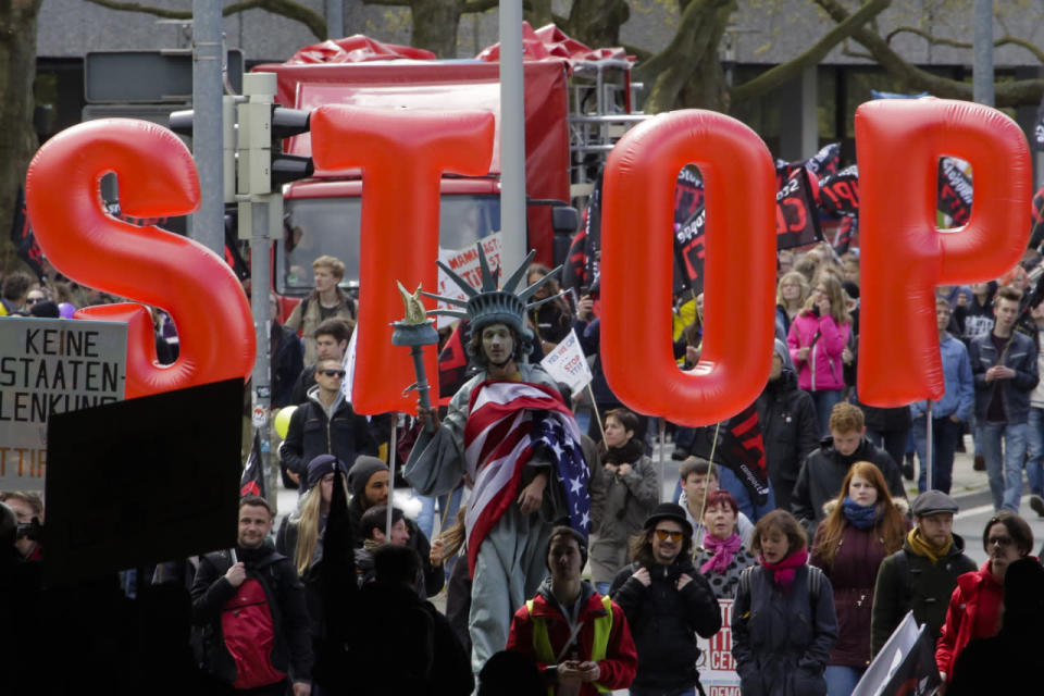 A man on stilts dressed like the Statue of Liberty walks in front of balloons forming the slogan “Stop TTIP” during a protest of thousands of demonstrators against the planned Transatlantic Trade and Investment Partnership (TTIP) and the Comprehensive Economic and Trade Agreement (CETA) ahead of a visit by President Obama in Hanover, Germany, April 23, 2016. (Markus Schreiber/AP)