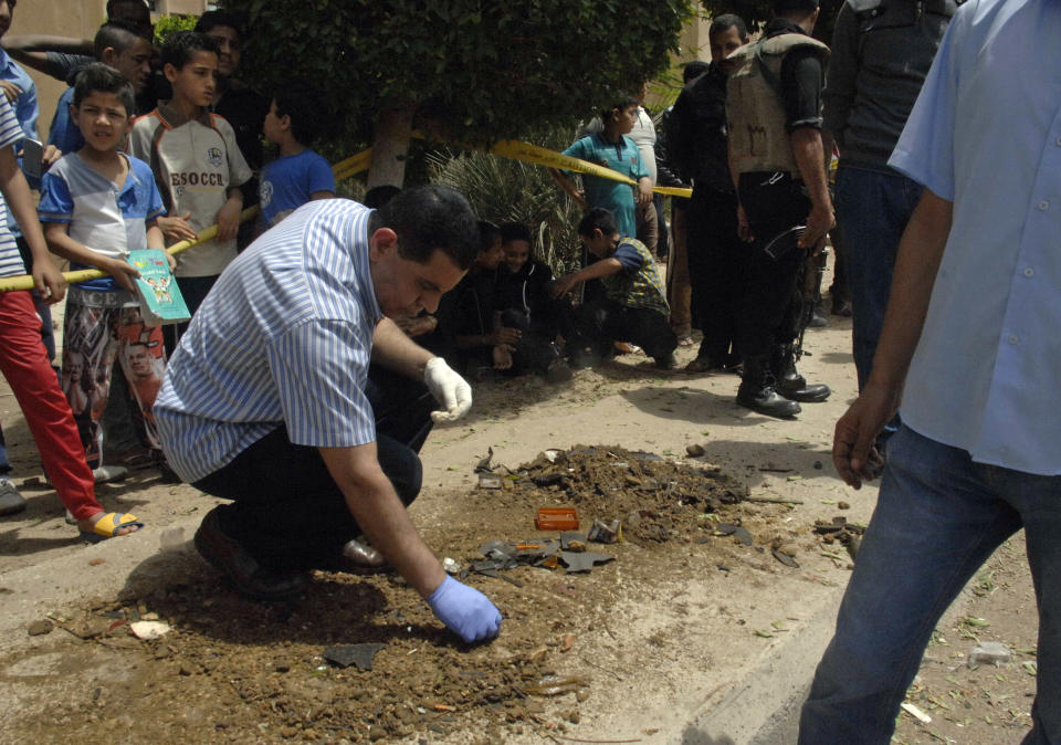 Security personnel search for clues at the site where senior Egyptian police officer Brig. Gen. Ahmed Zaki was killed after an explosive device placed under his car went off, in a western suburb of Cairo, Egypt, Wednesday, April 23, 2014. Another police officer died in a raid on a militant hideout in the country's second-largest city, Alexandria, officials said. The deaths came amid stepped-up attacks against Egyptian police and military as militant groups wage an increasingly violent campaign following the July 2013 ouster of Islamist President Mohammed Morsi. (AP Photo/Ahmed Gamil)