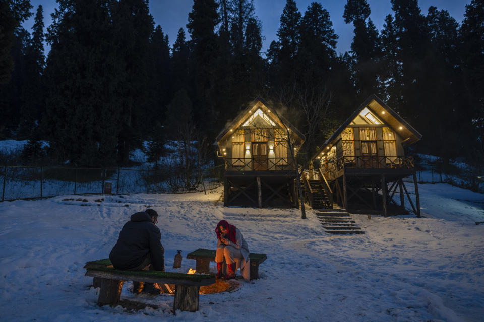 Tourists from Kenya sit by a bonfire outside a cottage in Drang village, northwest of Srinagar, Indian controlled Kashmir, Thursday, Dec. 21, 2023. This is the time of "Chillai Kalan," also called "The Great Winter," a Kashmiri phrase which defines the harshest 40 days of cold in disputed Kashmir that commence in late December and extend into January and early February. Renowned for its breathtaking landscapes, Kashmir in winter transforms into a wonderland. Tourists fill its hotels to ski, sledge and trek the Himalayan landscape.(AP Photo/Dar Yasin)