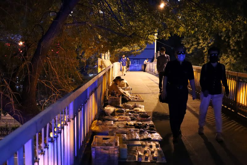 People walk past a street vendor waiting for customers at his stall on a footbridge in Beijing