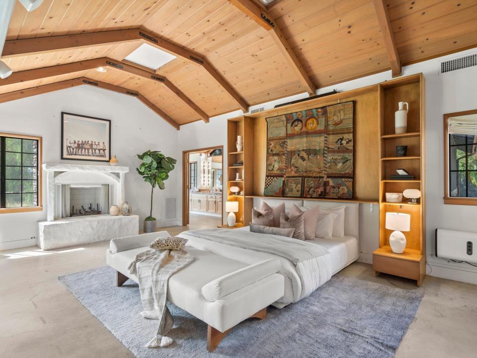 A large white walled bedroom with exposed wood beams and ceilings and a white bed