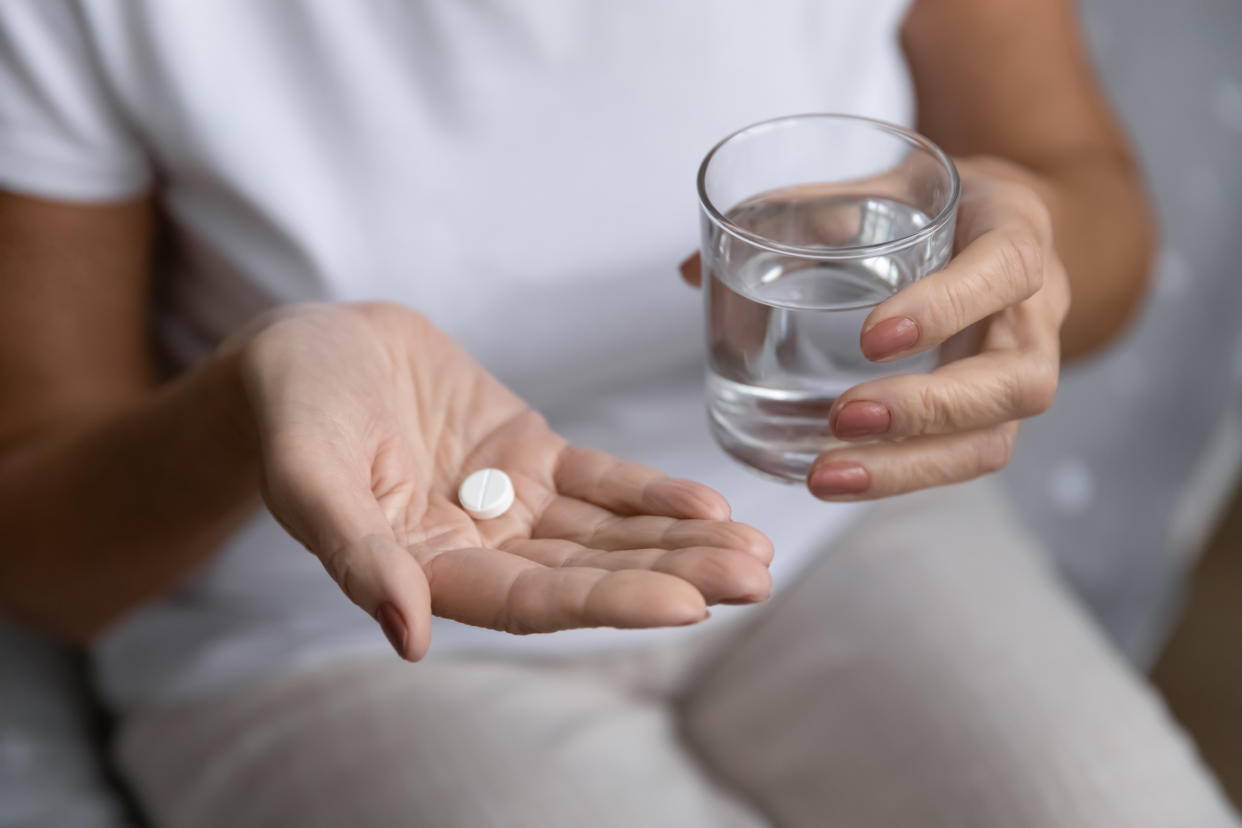 A close-up image of someone holding a pill in one hand and a glass of water in another.