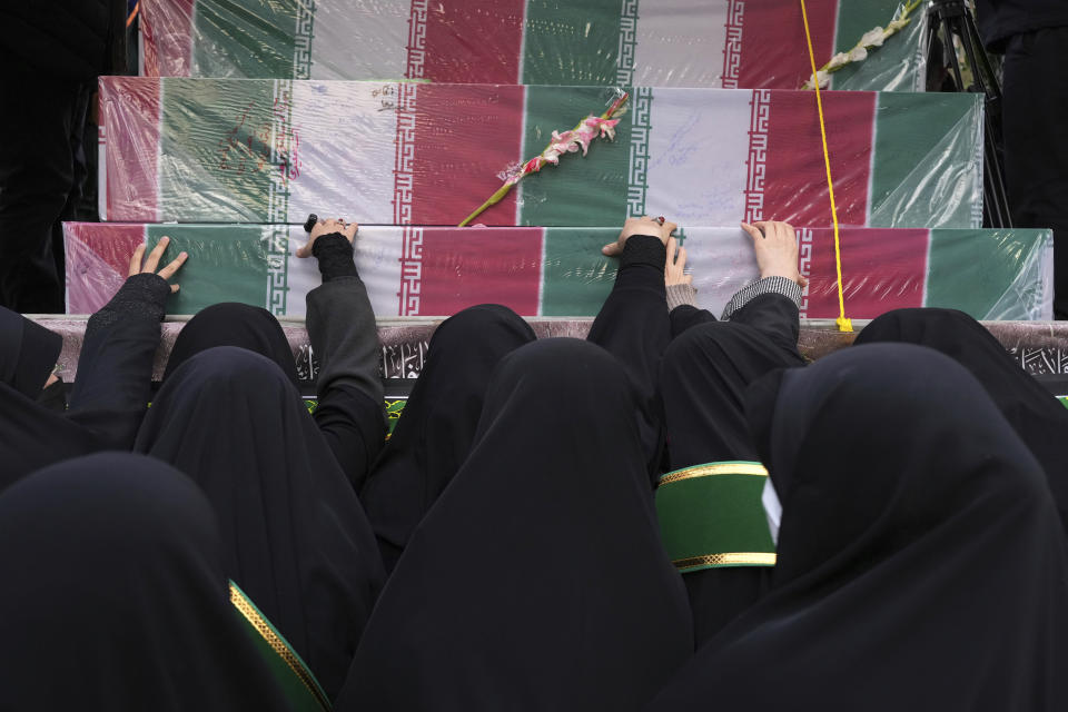 Mourners touch flag-draped coffins of unknown Iranian soldiers who were killed during the 1980-88 Iran-Iraq war, whose remains were recently recovered in the battlefields, during their funeral procession, in Tehran, Iran, Tuesday, Dec. 27, 2022. (AP Photo/Vahid Salemi)
