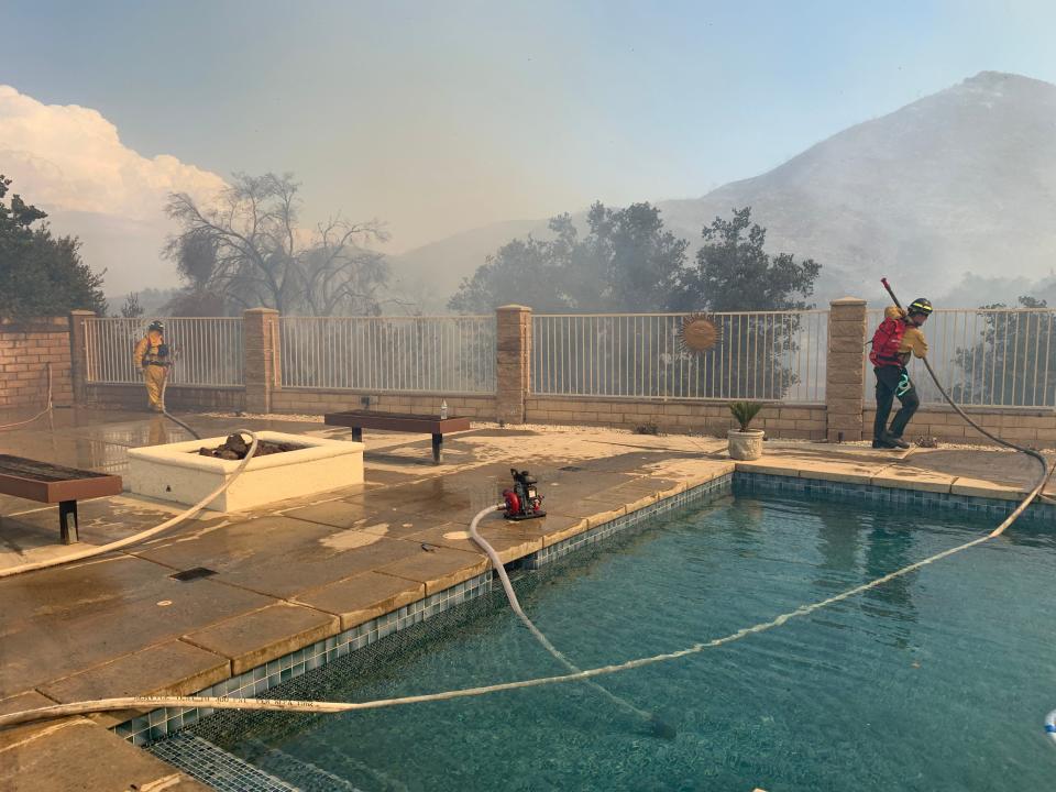 Two Wildland Defense Systems firefighters, privately contracted firefighters hired by the United Services Automobile Association, battle flames threatening an insured home in the Copper Canyon neighborhood of Murrieta, California, on Thursday, Sep. 5, 2019.