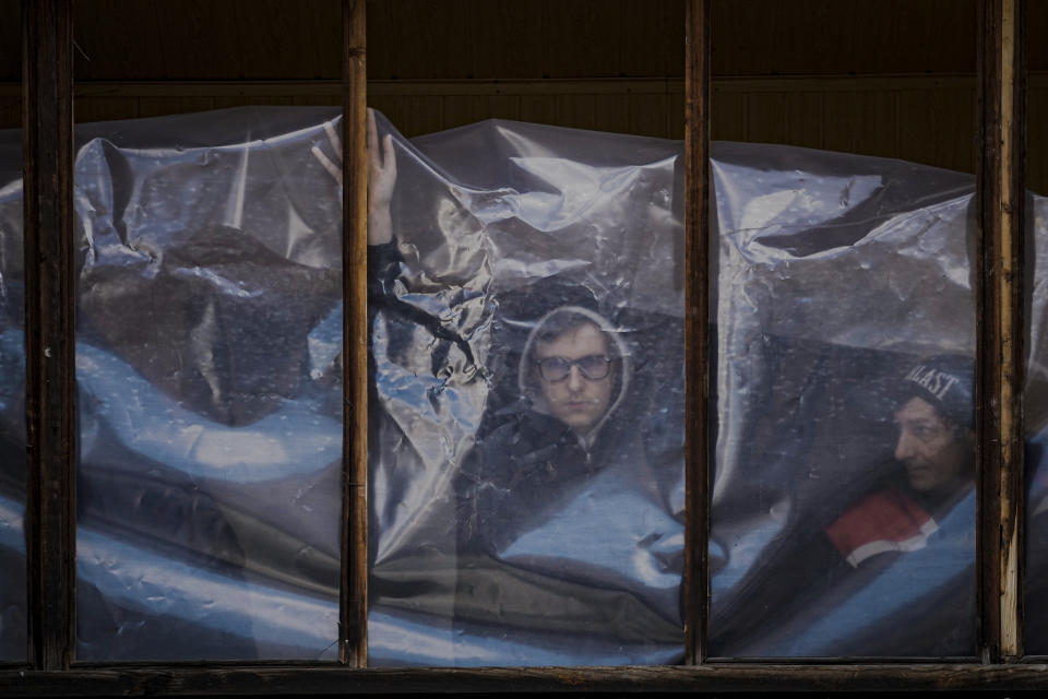 People put up plastic sheets to cover the broken windows of their apartments after parts of a Russian missile, shot down by Ukrainian air defense, landed on an apartment block, according to authorities, in Kyiv, Ukraine, Thursday, March 17, 2022. (AP Photo/Vadim Ghirda)