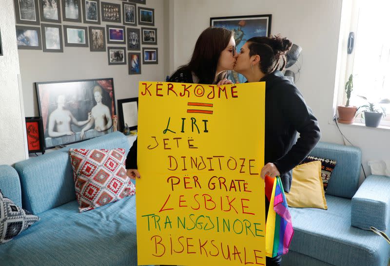 Xheni Karaj, an LGBT rights activist, kisses her girlfriend while holding a poster at their home in Tirana