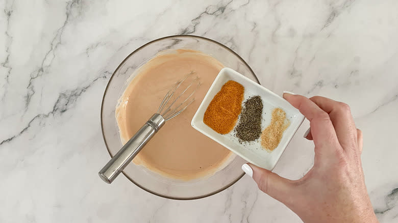 Hand holding spices on top of a bowl