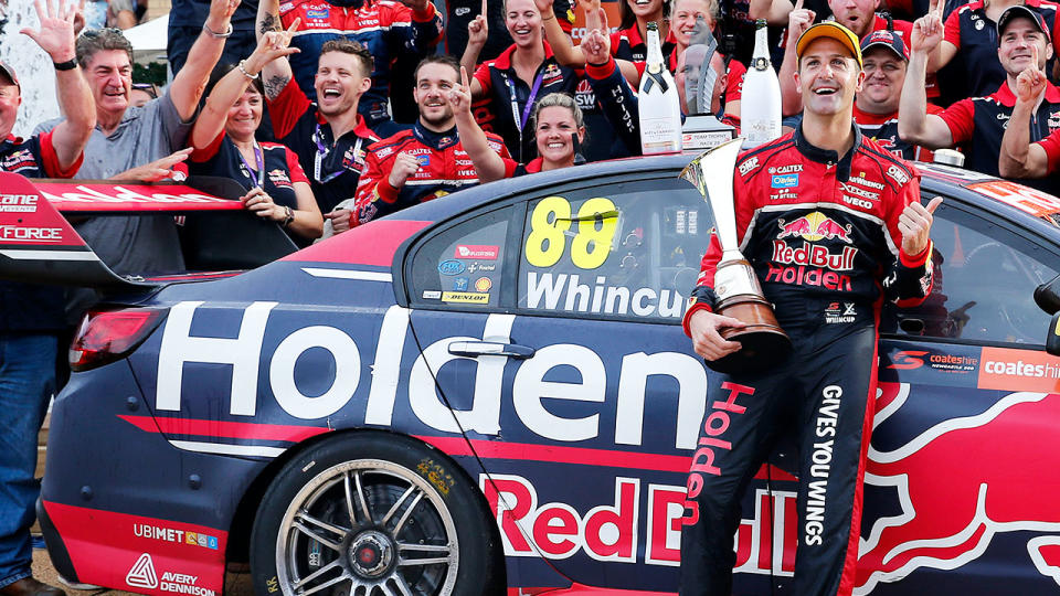 Red Bull Holden Racing Team driver Jamie Whincup holds trophy and leans on Holden car.