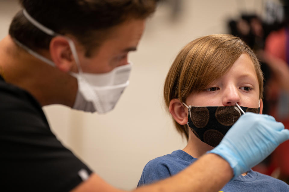 A health care worker wearing a face mask and rubber gloves, inserts a swab into the nose of student.