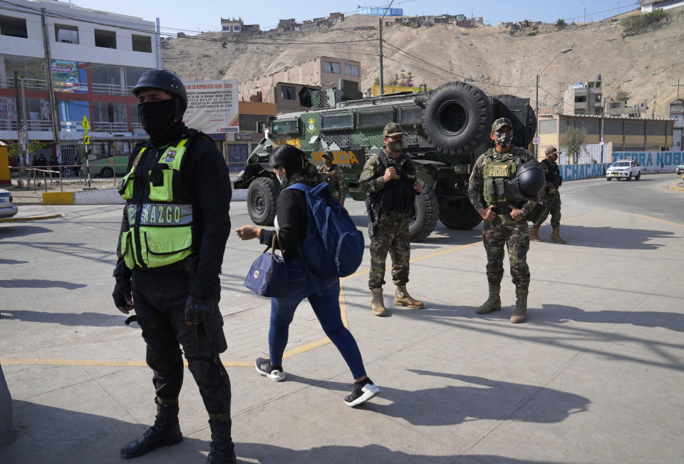 A woman walks past Special Forces Police at a checkpoint in the Manchay district, on the outskirts of Lima, Peru, Tuesday, April 5, 2022. Peru’s President Pedro Castillo imposed a tight curfew on the capital and the country’s main port in response to sometimes violent protests over rising prices of fuel and food, requiring people in Lima and Callao to mostly stay in their homes all of Tuesday. (AP Photo/Martin Mejia)