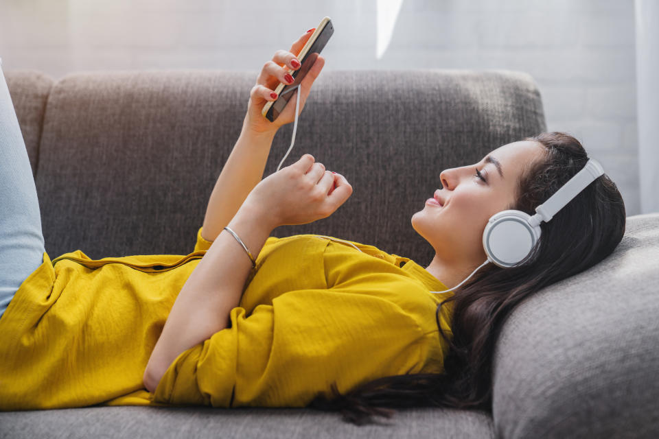 Side view of young woman listening to music online on smartphone in headphones