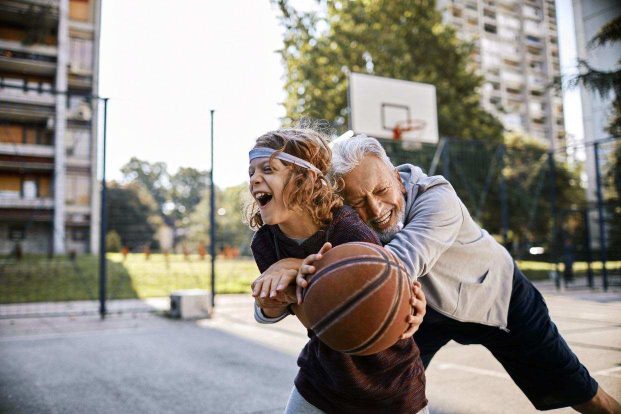 senior man hugging grandchild, playing basketball together