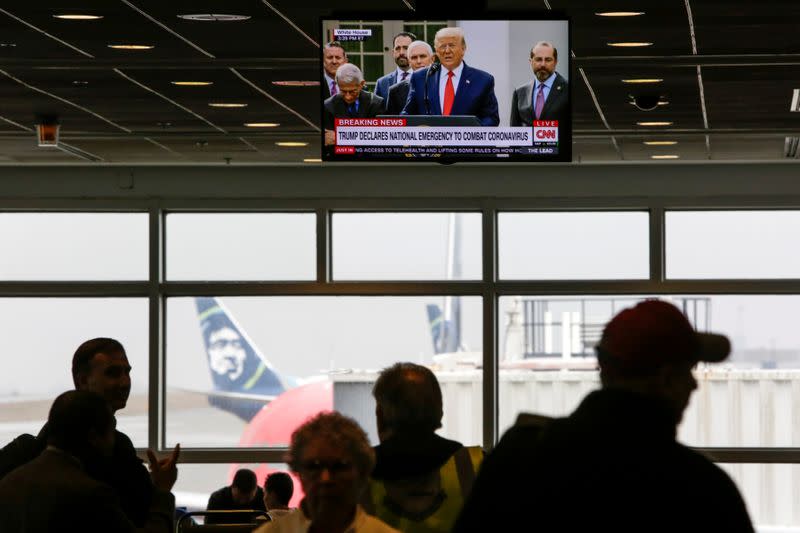 Travelers watch as U.S. President Donald Trump is pictured on a television at Seattle-Tacoma International Airport as he declares a national emergency over the coronavirus, in SeaTac Washington