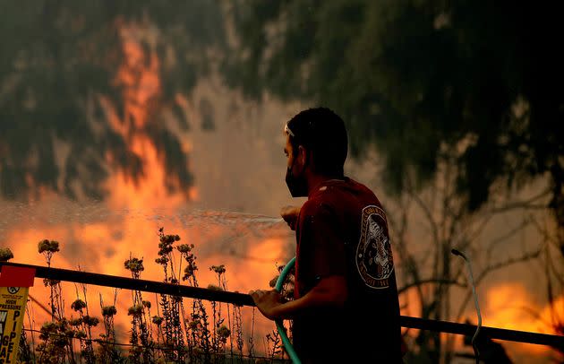 A man uses a garden hose to water down dry vegetation as the Alisal fire burns at the edges of a ranch near Goleta, California, on Oct. 12. (Photo: Luis Sinco via Getty Images)