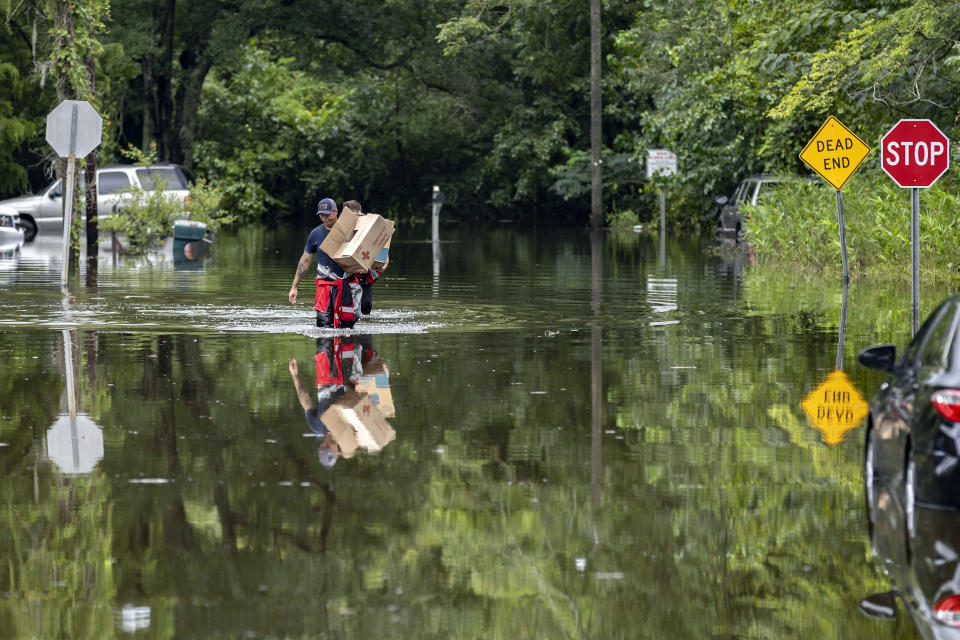 Savannah Fire Advanced Firefighters Andrew Stevenson, front, and Ron Strauss carry food to residents in the Tremont Park neighborhood that where stranded in flooding from Tropical Storm Debby, Tuesday, Aug. 6, 2024, in Savannah, Ga. (AP Photo/Stephen B. Morton)