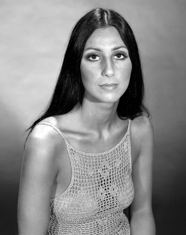Cher in a crochet top, with long straight hair, posing for a portrait against a plain background