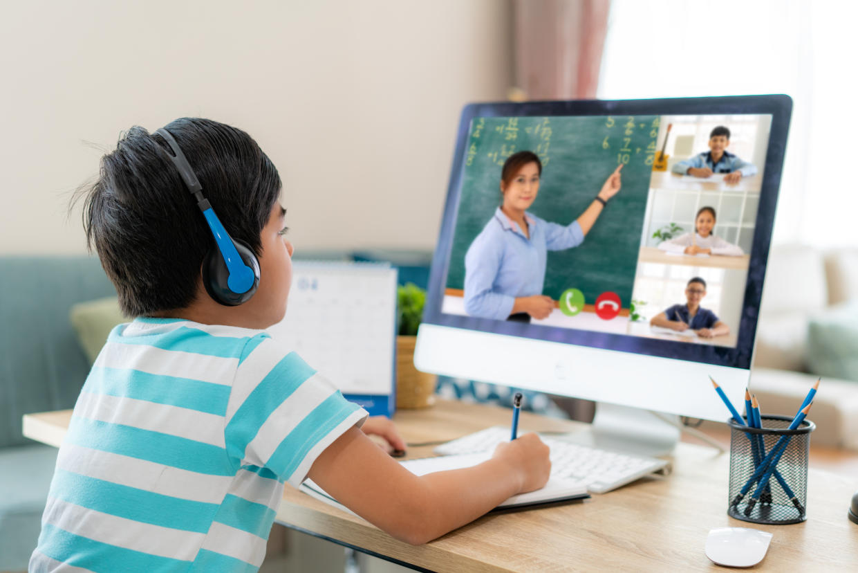 A student at home wearing headphones pays attention during a video conference e-learning session with a teacher and his classmates.