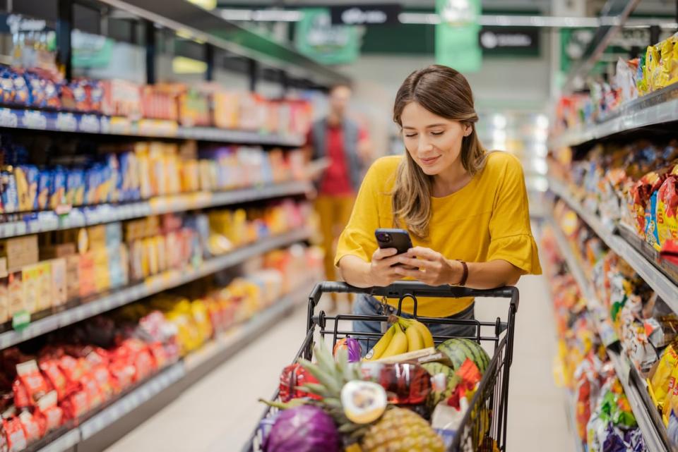 A person pushing ⁢a‍ shopping cart through a store while on their phone.