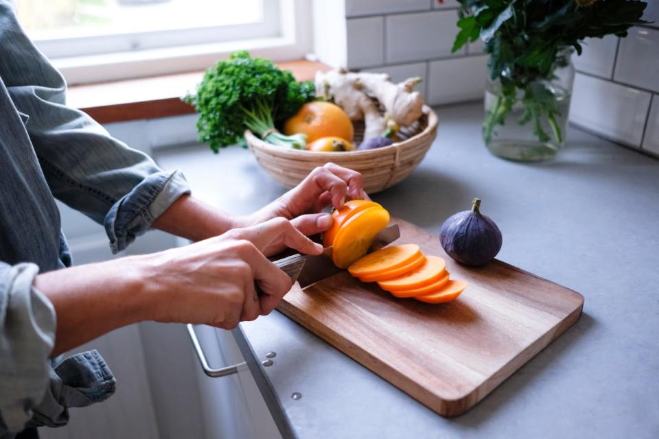 A woman slices a persimmon on a cutting board