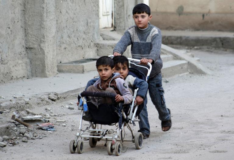 A boy carries two younger boys in a pushchair on February 8, 2014 in a street of the northeastern Syrian city of Deir Ezzor