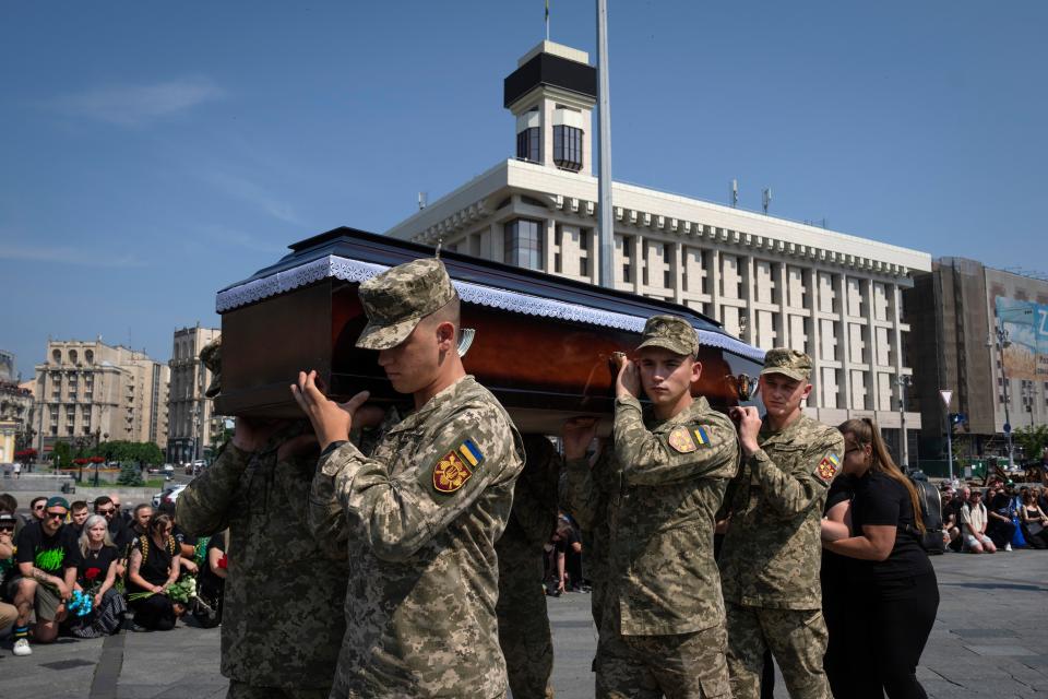 People kneel as servicemen carry the coffin of volunteer soldier Ivan Shulga, a sound producer in TV channels and musician, killed in a battle with the Russian troops near Bakhmut (AP)