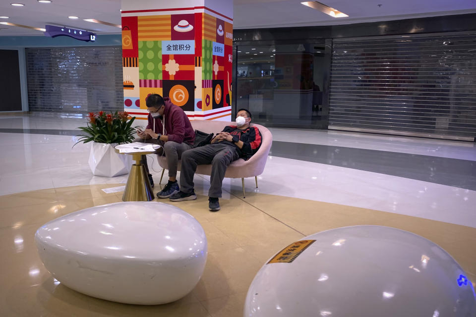 Men wearing face masks sit on a bench seat near empty storefronts at a shopping mall in Beijing, Wednesday, Oct. 12, 2022. A meeting of the ruling Communist Party to install leaders gives President Xi Jinping, China's most influential figure in decades, a chance to stack the ranks with allies who share his vision of intensifying pervasive control over entrepreneurs and technology development. (AP Photo/Mark Schiefelbein)