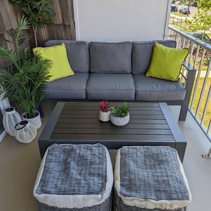 Outdoor furniture set with a sofa, table, cushions, and plants on a balcony