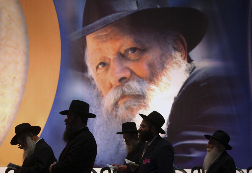 FILE - Backdropped by a huge poster showing Lubavitcher rabbi Menachem Mendel Schneerson, a group of Jewish Orthodox men pray during a ceremony marking the 10th anniversary of his passing in Yad Eliyahu stadium in Tel Aviv, Israel, Monday June 21, 2004. Members from the Chabad Hasidic sect crowded into the stadium for the memorial ceremonies. (AP Photo/Ariel Schalit, File)