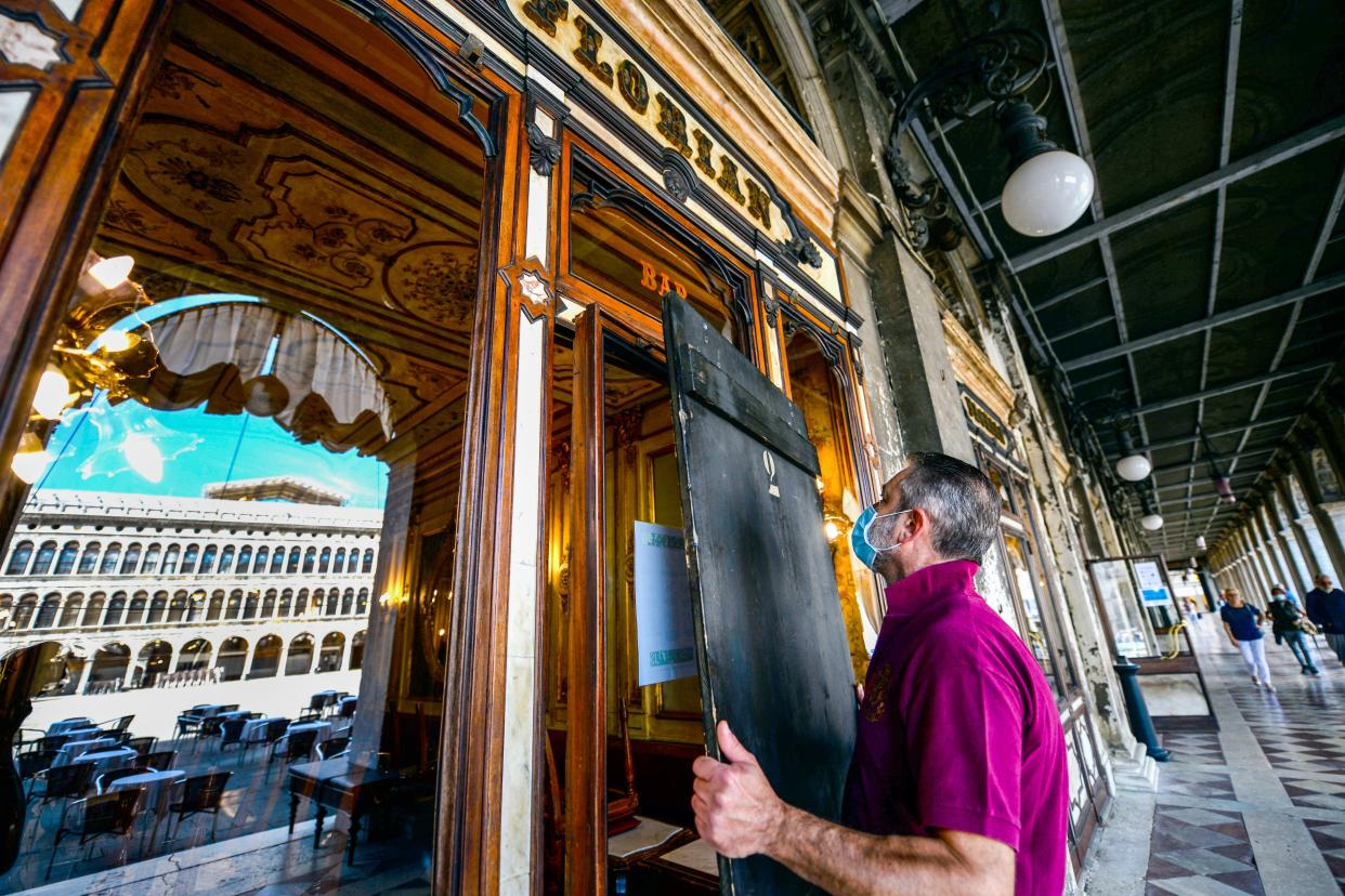 An employee takes off wooden shutters from the facade of 18th Century Cafe Florian on June 12, 2020 on St. Mark's Square in Venice, which reopened after being closed for three months during the country's lockdown.