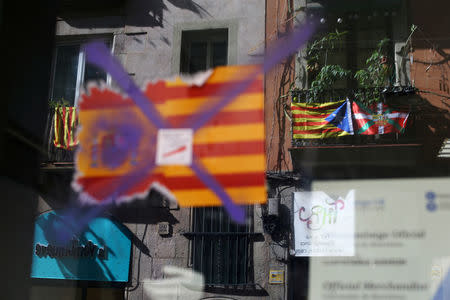 A Basque and a separatist Catalan flag are reflected in a window with a defaced sticker of the Spanish and Catalan flags in Barcelona, Spain, October 11, 2017. REUTERS/Ivan Alvarado