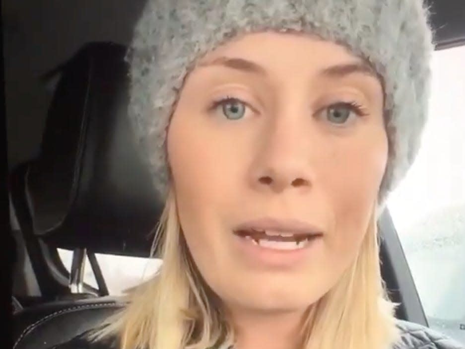 screenshot of a woman in a car wearing a hat and speaking to the camera