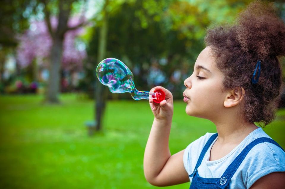 Child (7-8) Blowing Bubbles in Playground.